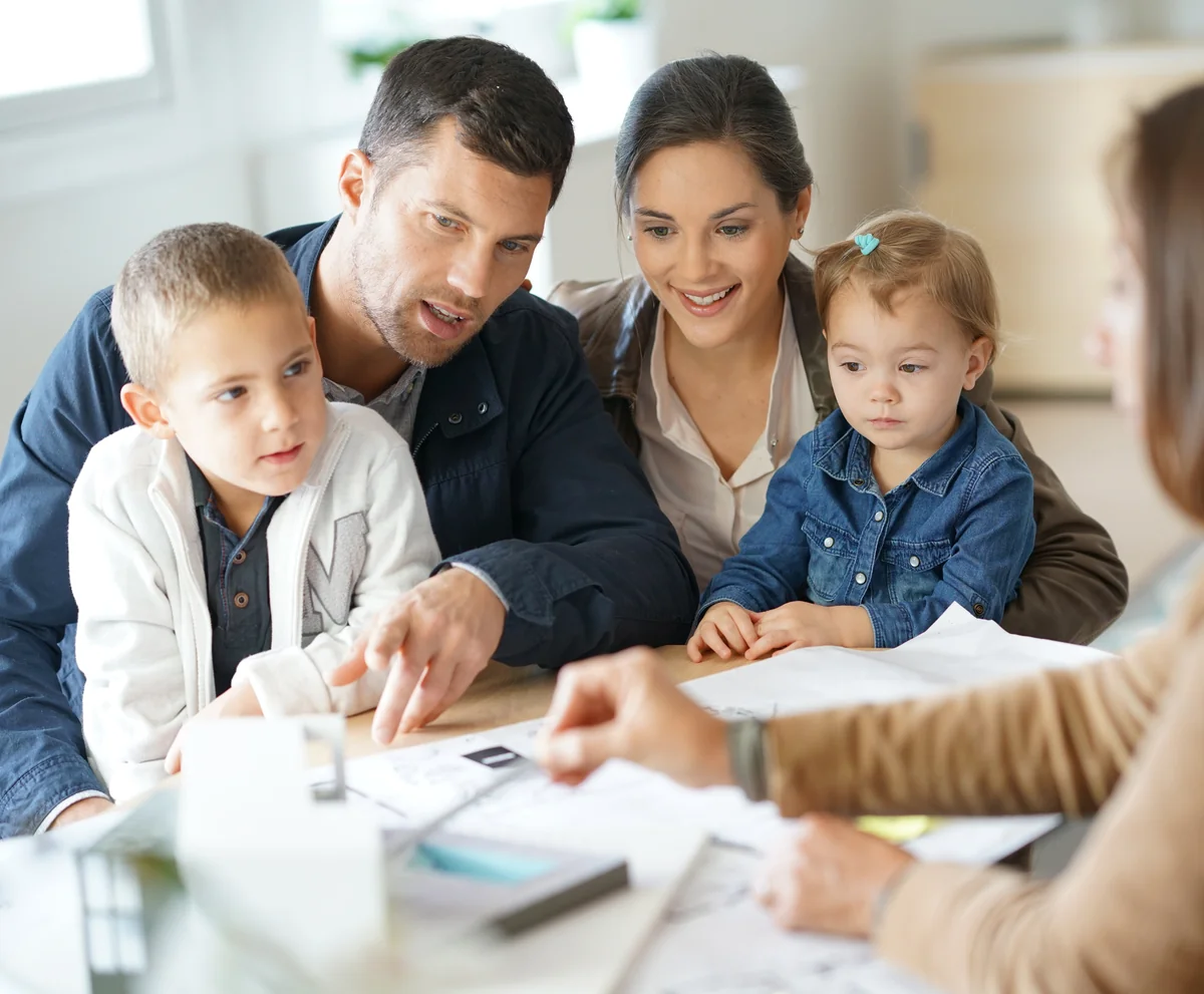 Familie mit zwei Kindern im Beratungsgespräch zur Eigenheimfinanzierung mit einer Finanzberaterin