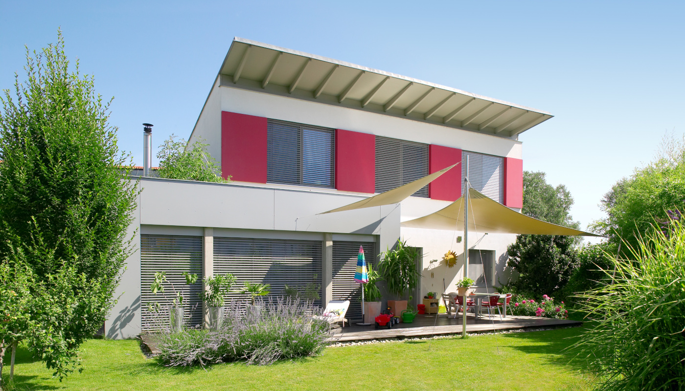 Modernes Einfamilienhaus mit Sonnensegeln über Terasse.