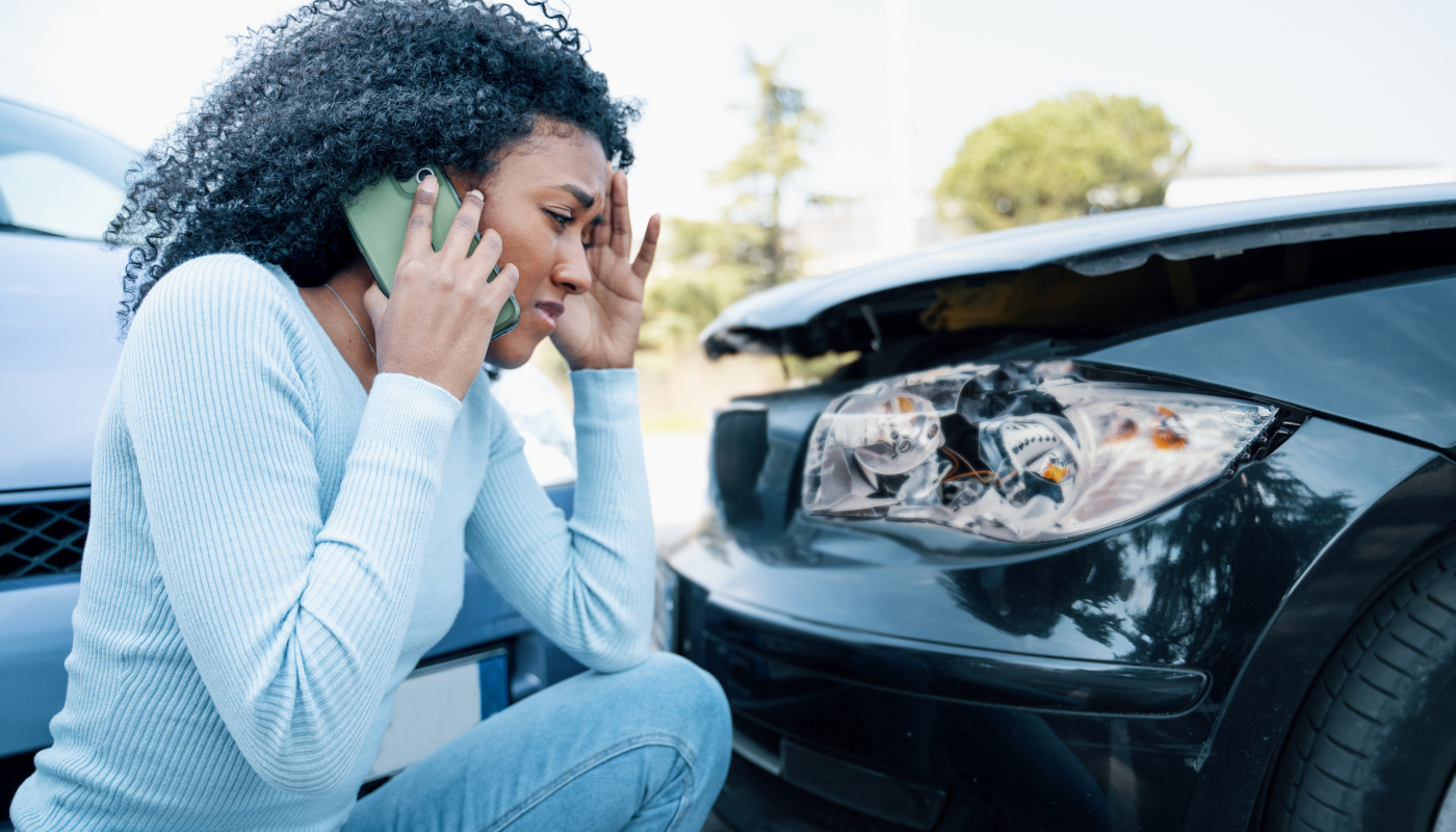 Junge Frau telefoniert neben ihrem bei einem Unfall beschädigten Auto.